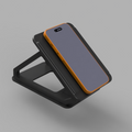 A black smartphone stand with an orange accent trim, holding a gray smartphone, shown on a solid gray background.