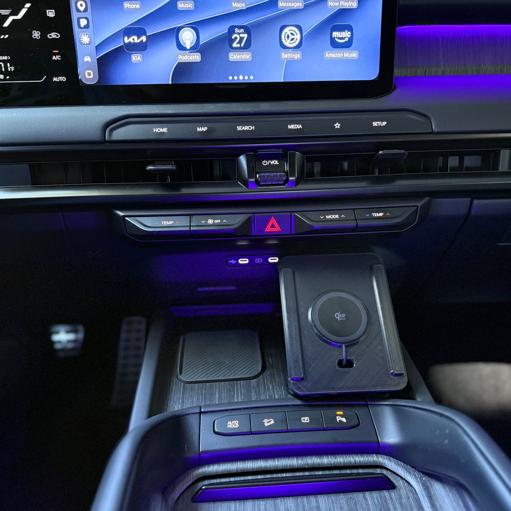 Close-up of a car interior console with a large illuminated touchscreen, center console controls, a wireless charging pad, and ambient purple lighting.